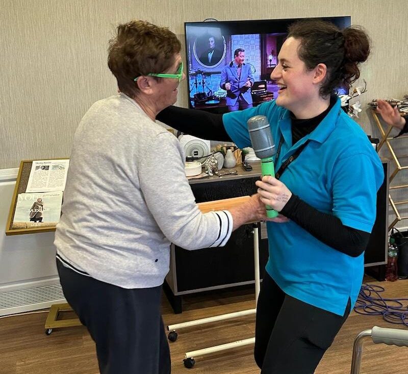 resident and activities coordinator dancing together in the lounge with blow up microphone